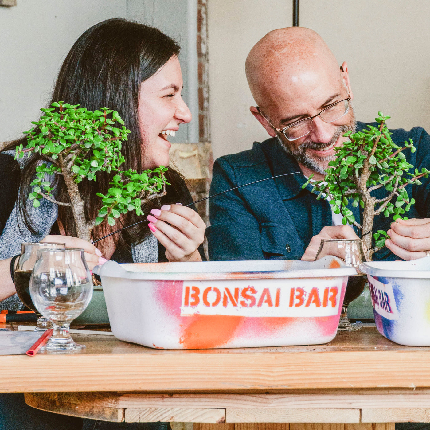 Friends learning to shape bonsai trees at a Bonsai Bar workshop